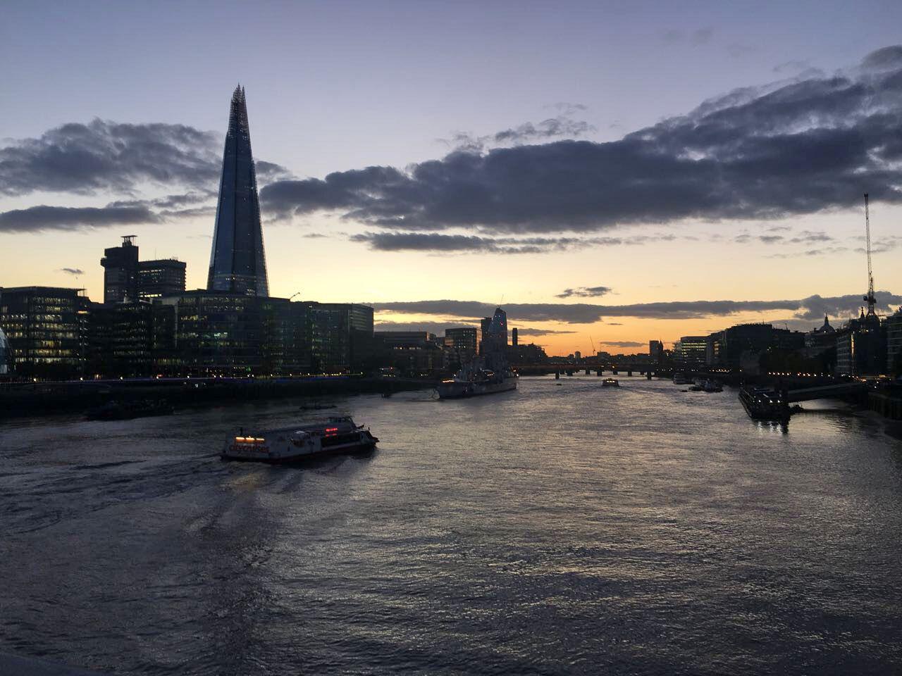 Abendliche Skyline mit The Shard und beleuchteten Gebäuden am Flussufer in London, Stadtansicht mit Booten.