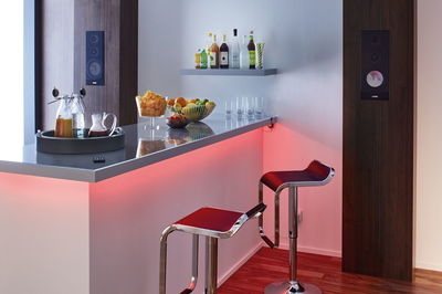 Moderne bar med rød LED-belysning, to røde barstole og mørke væghøjttalere