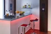 Moderne Bar mit roten LED-Leisten, zwei schwarzen Barhockern und Holzlautsprechern an der Wand