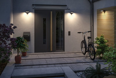 Trois appliques murales noires modernes avec lumière blanc chaud à l'entrée de la maison avec vélo et plantes.