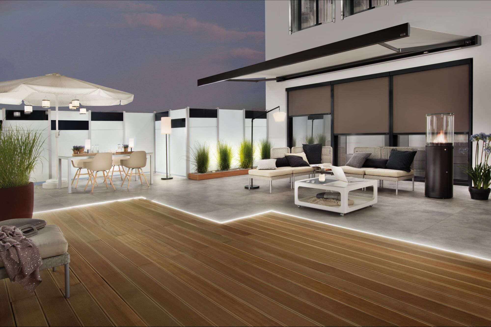 Moderne terras met LED-vloerverlichting, beige loungesofa, parasol en buiten eettafel met stoelen.