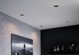 Four round recessed spotlights in white ceiling illuminate modern living room with grey wall and black shelf.