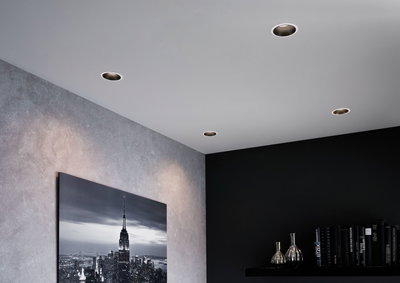 Vier ronde inbouwspots in wit plafond verlichten moderne woonkamer met grijze muur en zwarte plank.
