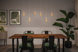 Moderne spisestue med træbord, sorte metalstole og varme LED-hængelamper til boligbelysning.