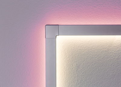 Hoekdetail van zilveren LED-wandlamp met warm wit licht en roze achtergrondverlichting