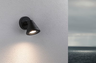 Black metal outdoor wall light with warm white LED on white wall overlooking the sea