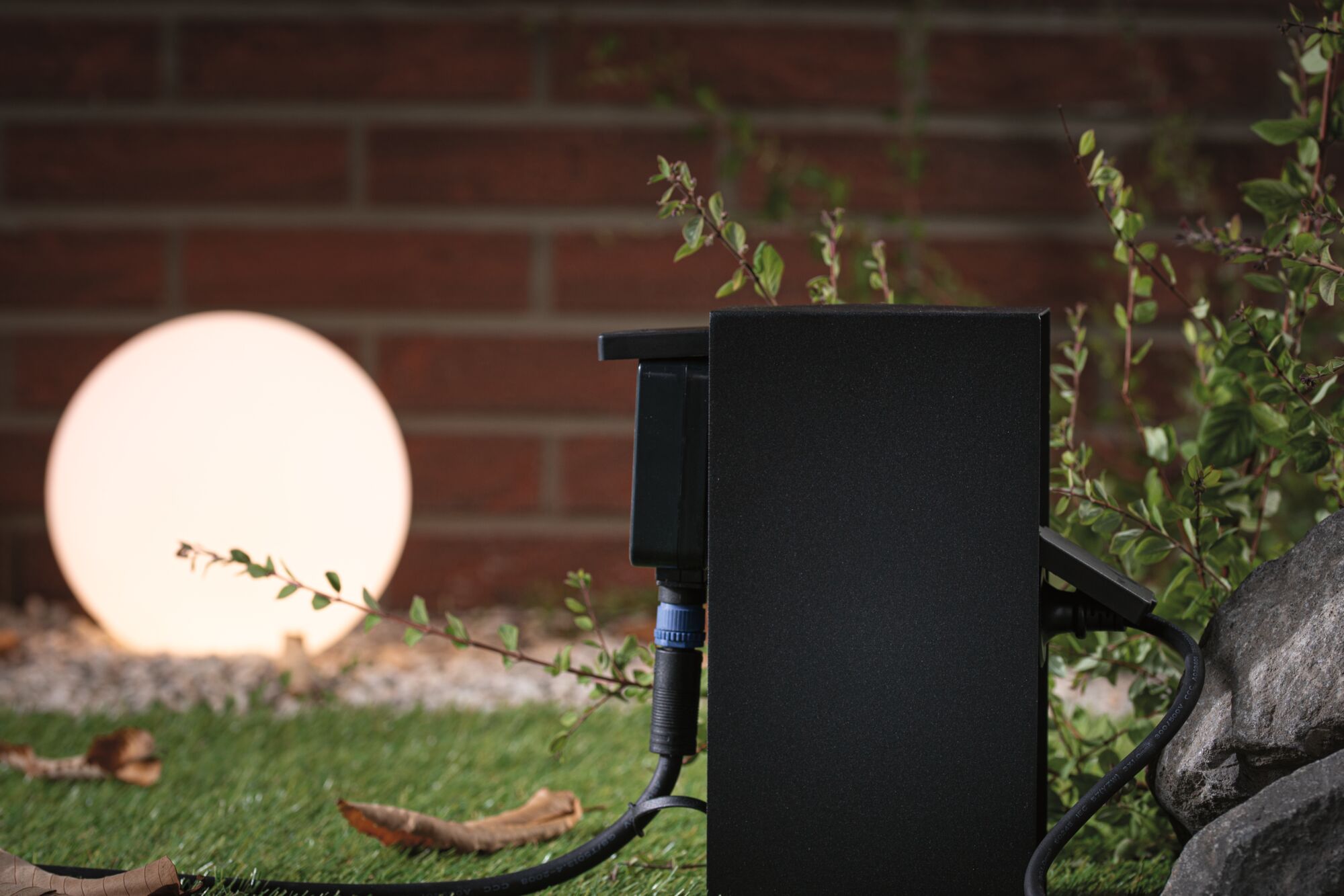 Zwarte buitenbehuizing met kabelverbinding voor verlichte ronde tuinlamp op gras.