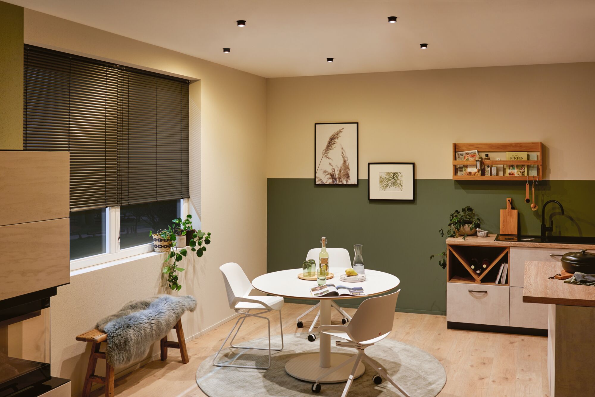 Moderne eetruimte met ronde witte tafel en stoelen, houten vloer, groen-beige muur en plafondspots