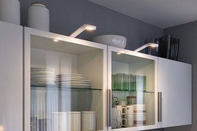 Witte keukenkasten met glazen deuren verlicht door moderne LED-spots met servies en glazen.