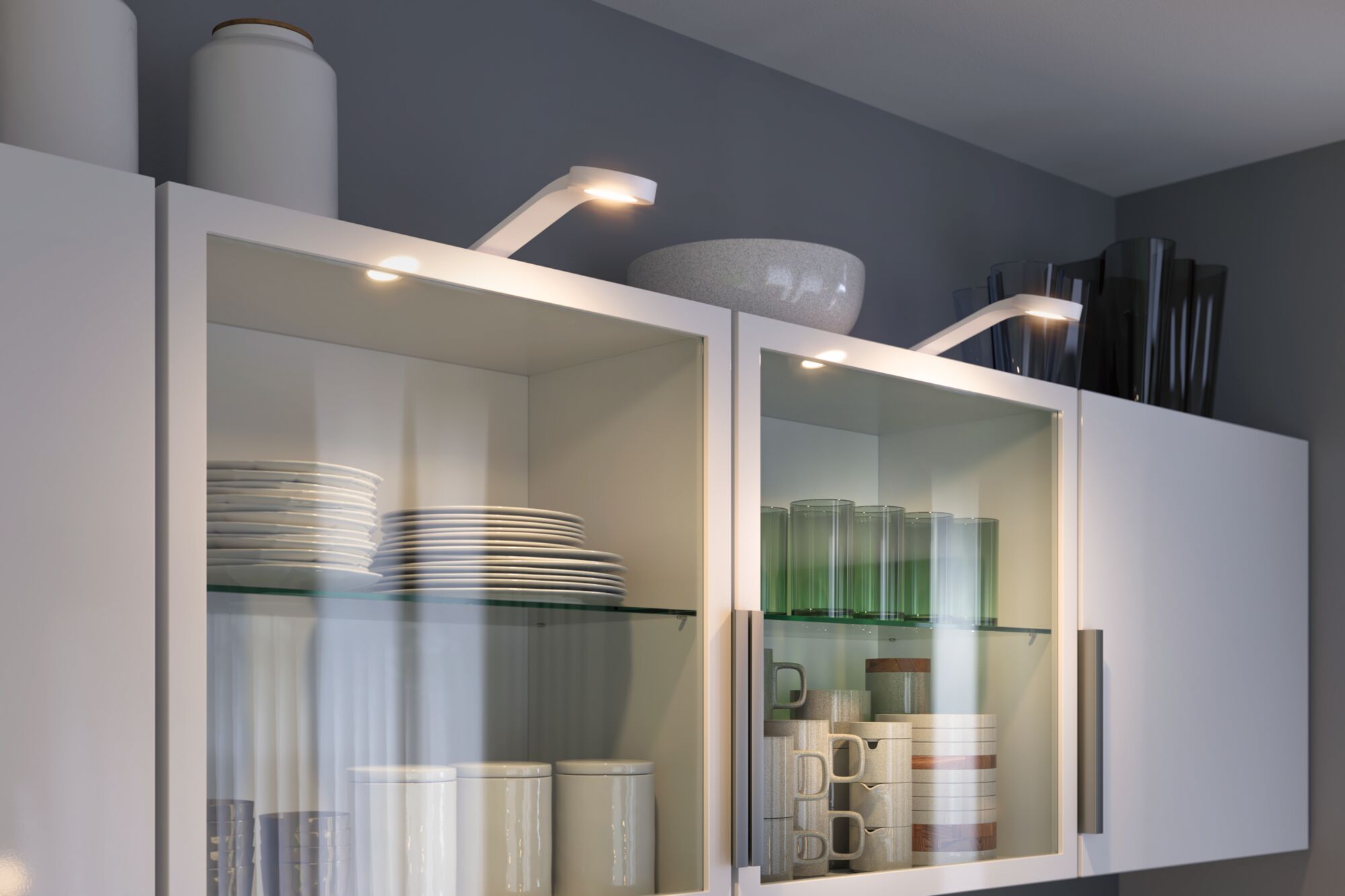 Weiße Küchenschränke mit Glasfront, beleuchtet von modernen LED-Spots, zeigen Geschirr und Gläser.