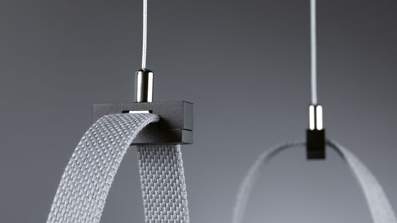 Close-up van grijze textielband met zwarte metalen clip en witte kabel op grijze achtergrond