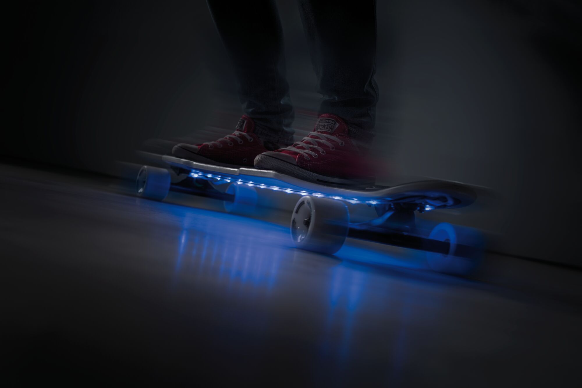 Skateboard avec lumières LED bleues sous plateau transparent et baskets rouges dans l'obscurité