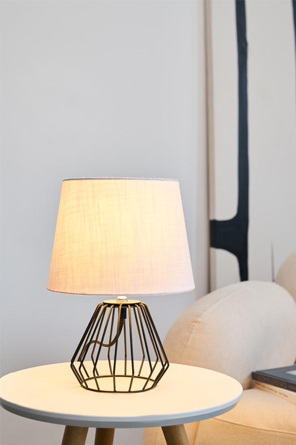 Modern table lamp with black metal frame and light fabric shade on white side table in living room
