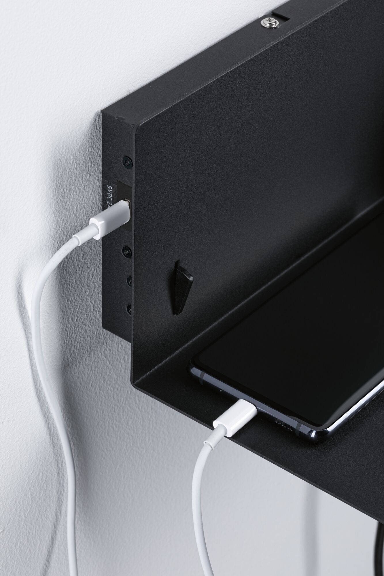 Black metal wall shelf with smartphone and white charging cable for convenient charging station