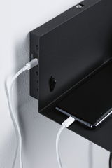 Black metal wall shelf with smartphone and white charging cable for convenient charging station