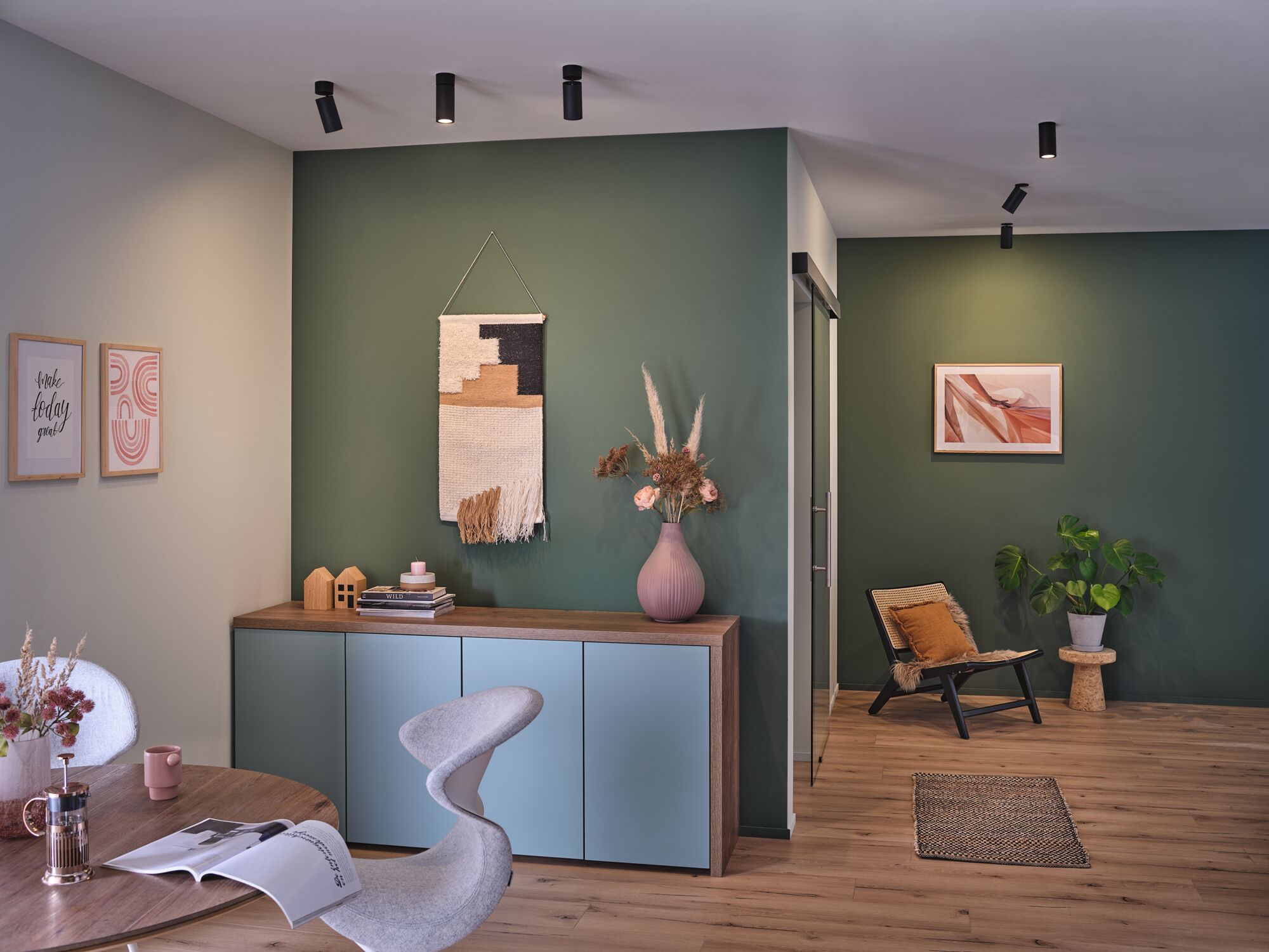 Moderne woonkamer met groene muur, houten dressoir, grijze stoel en zwarte plafondspots voor accentverlichting