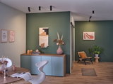 Salon moderne avec mur vert, buffet en bois, chaise grise et spots noirs au plafond pour éclairage d'accent