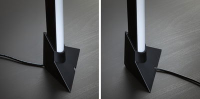 Black LED floor lamp with white light tube and cable on dark wooden floor for modern room lighting