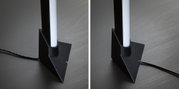 Schwarze LED-Stehleuchte mit weißem Leuchtstab und Kabel auf dunklem Holzboden für moderne Raumbeleuchtung