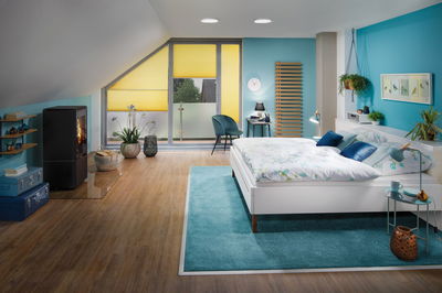 Chambre moderne avec lit blanc, tapis bleu, stores plissés jaunes et sol en bois pour une ambiance chaleureuse