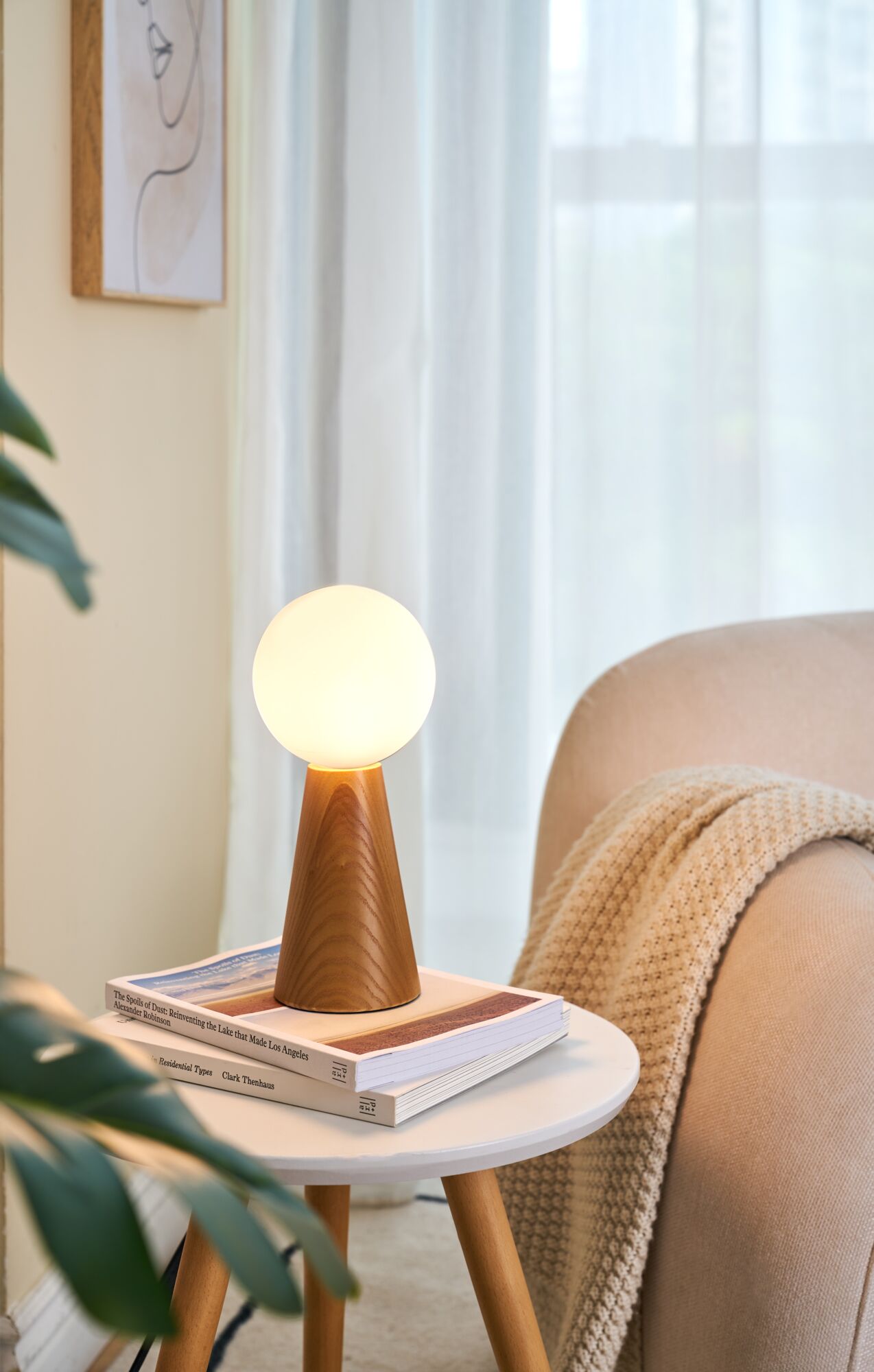 Moderne bordlampe med træfod og rund hvid glas på sidebord i hyggelig stueindretning.