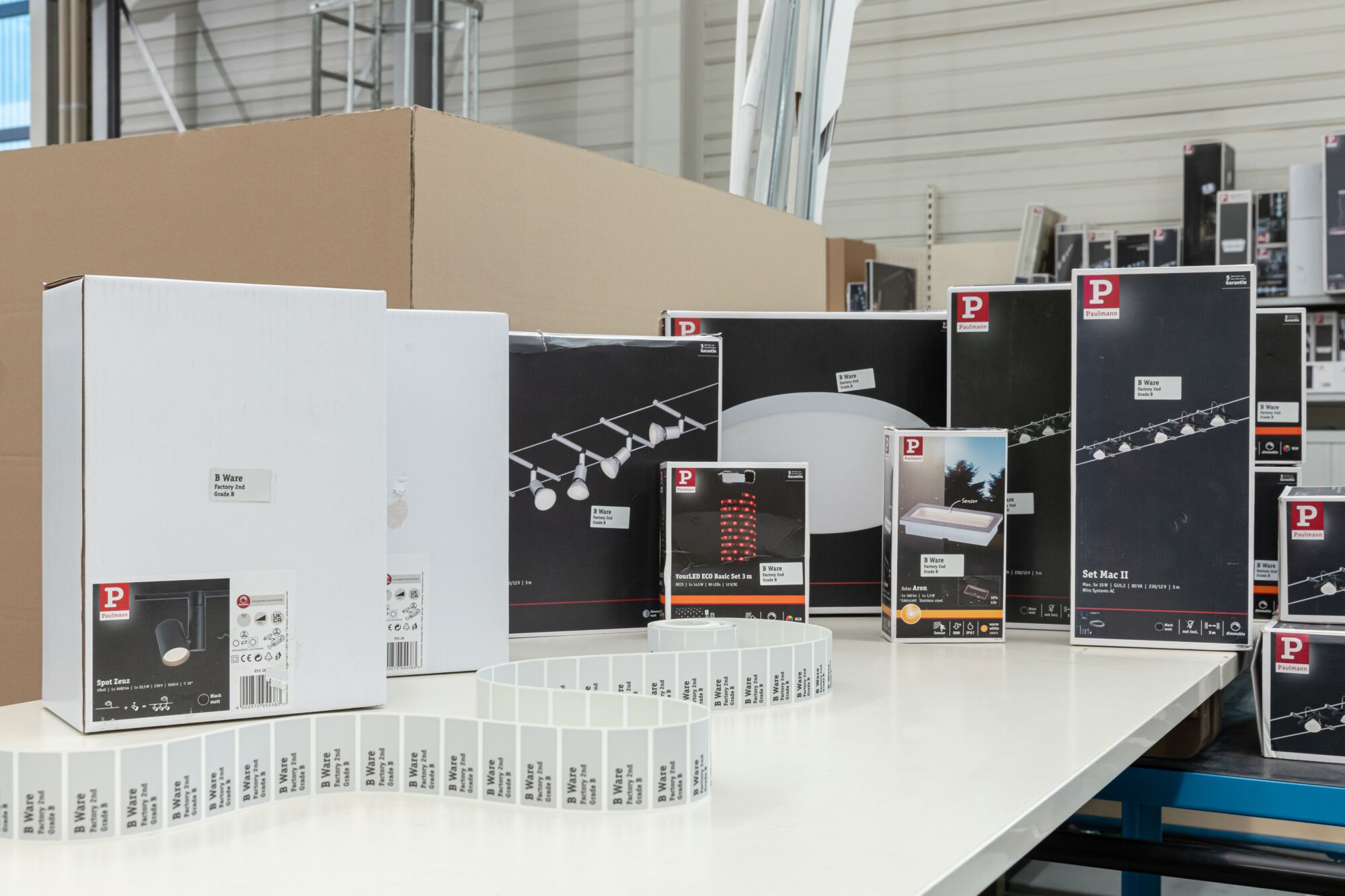 Diverse Paulmann verlichtingsproducten in dozen met B-ware labels op tafel in magazijnomgeving