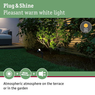 Outdoor spotlight with warm white light illuminating green plants by wooden fence in garden at night