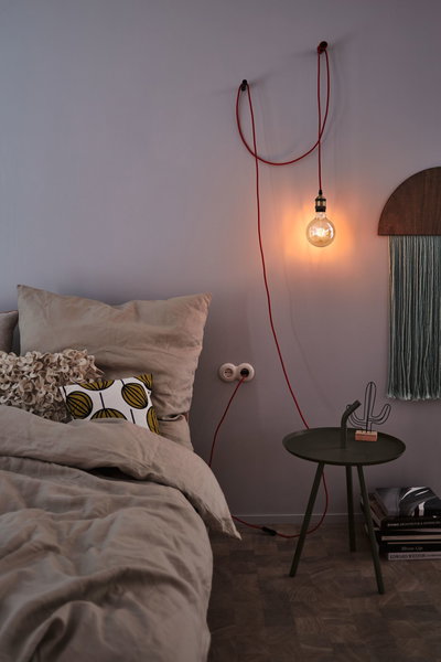 Slaapkamer met grijze muur, rode hanglamp met gloeilamp, groene bijzettafel met decoratie en boeken