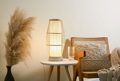 Natuurlijke houten tafellamp met warm licht op witte bijzettafel naast stoel met macramé kussen