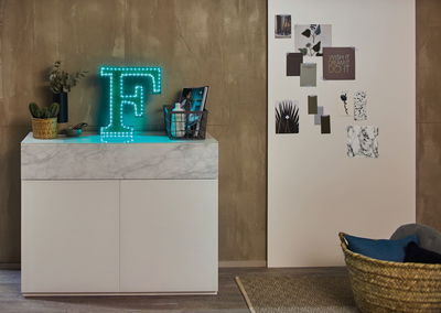 Leuchtender Buchstabe F mit blauen LED-Lichtern auf weißem Sideboard mit Marmoroptik im Wohnzimmer