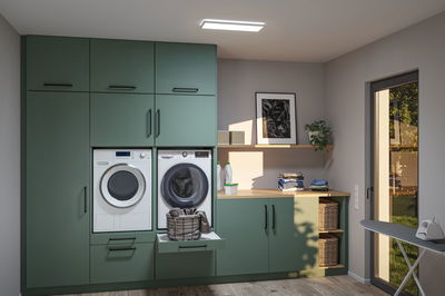 Moderne grüne Küchenzeile mit Waschmaschine, Trockner und Wäschekorb in hellem Hauswirtschaftsraum