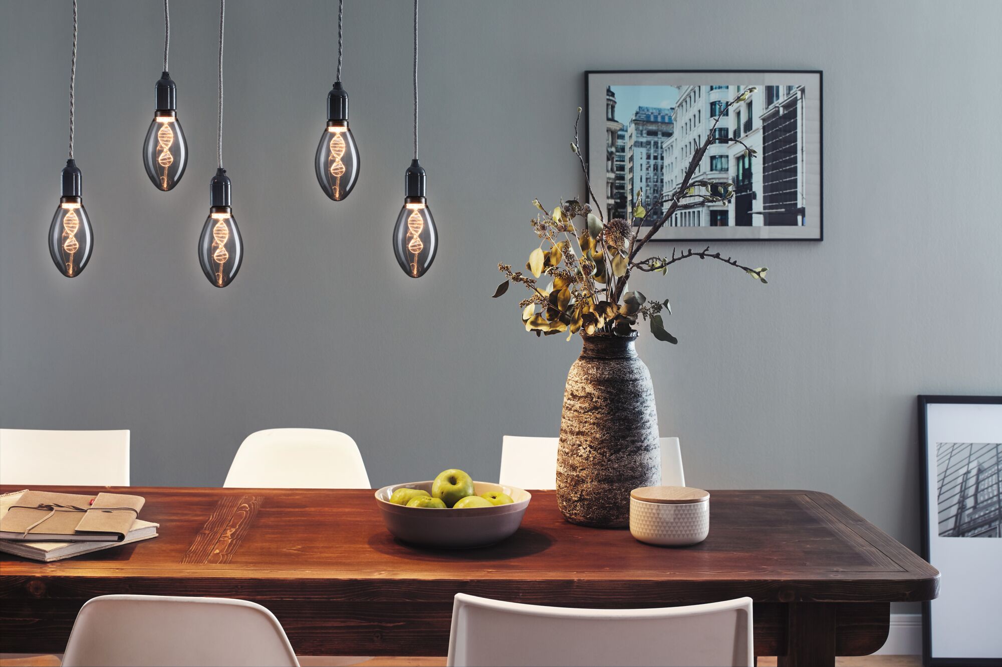 Five hanging LED bulbs with DNA filament above wooden table with vase and green fruit in dining room