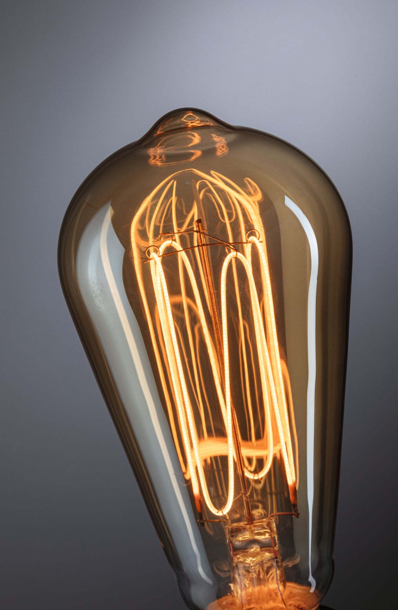 Nærbillede af varmglødende vintage-pære med brunt glas og synligt LED-filament til dekorativ belysning.