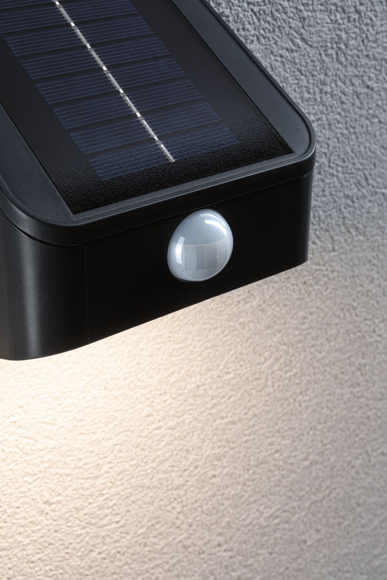 Black plastic solar light with motion sensor mounted on textured wall for outdoor lighting