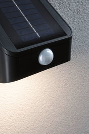Black plastic solar light with motion sensor mounted on textured wall for outdoor lighting