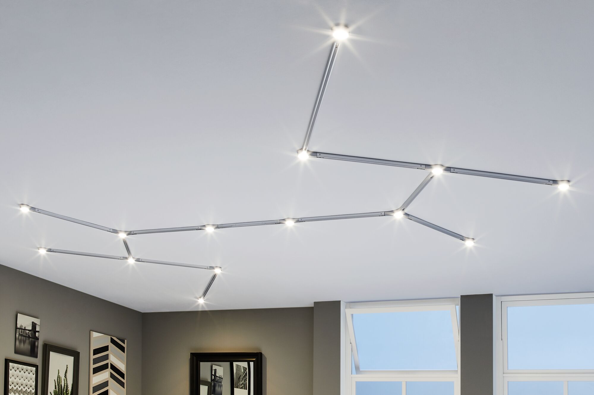 Modular silver LED track lighting with warm white light on white ceiling in living room.