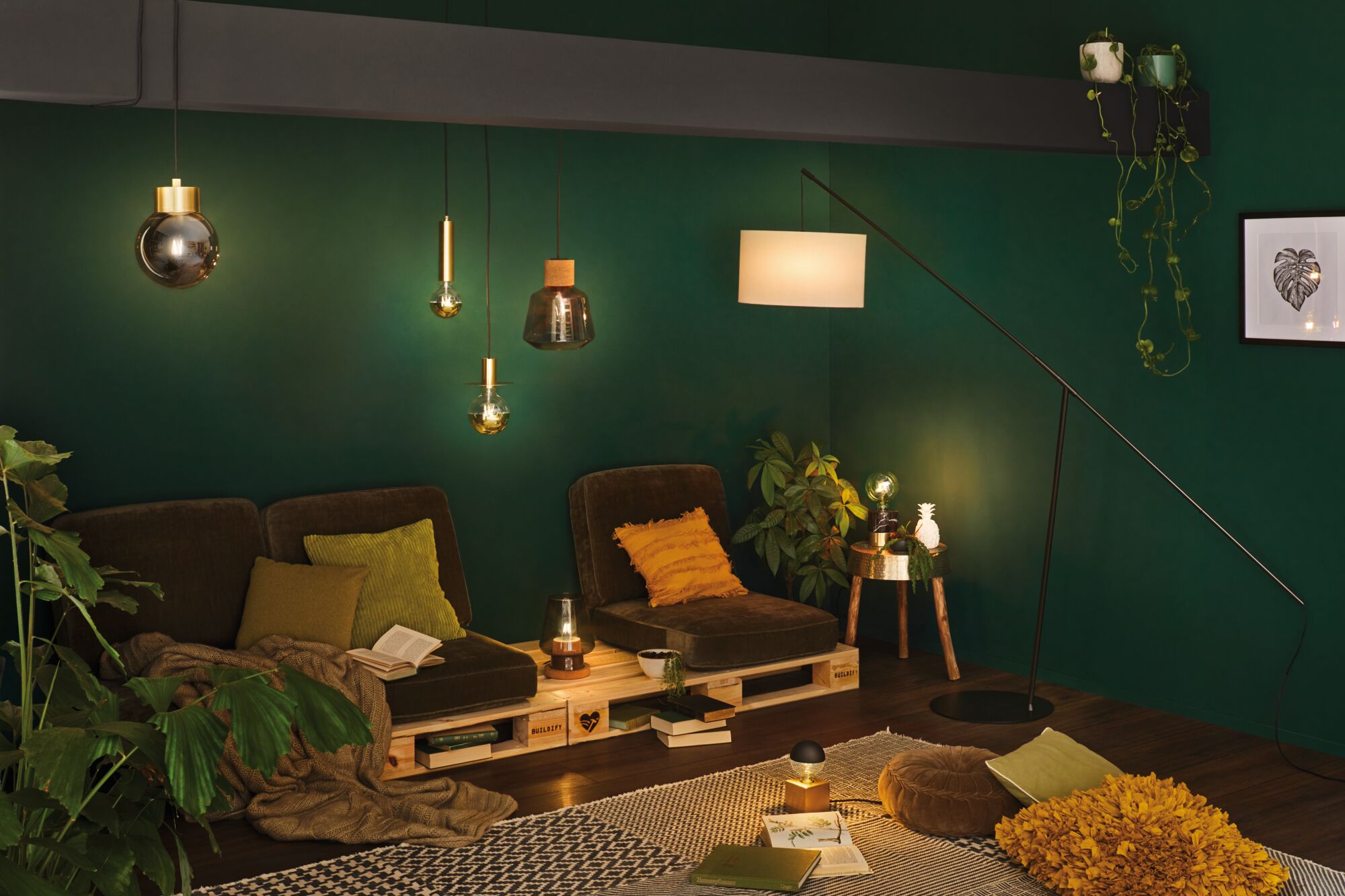 Woonkamer met groene muur, bruine fauteuils, houten pallet als tafel en moderne glazen en metalen hanglampen