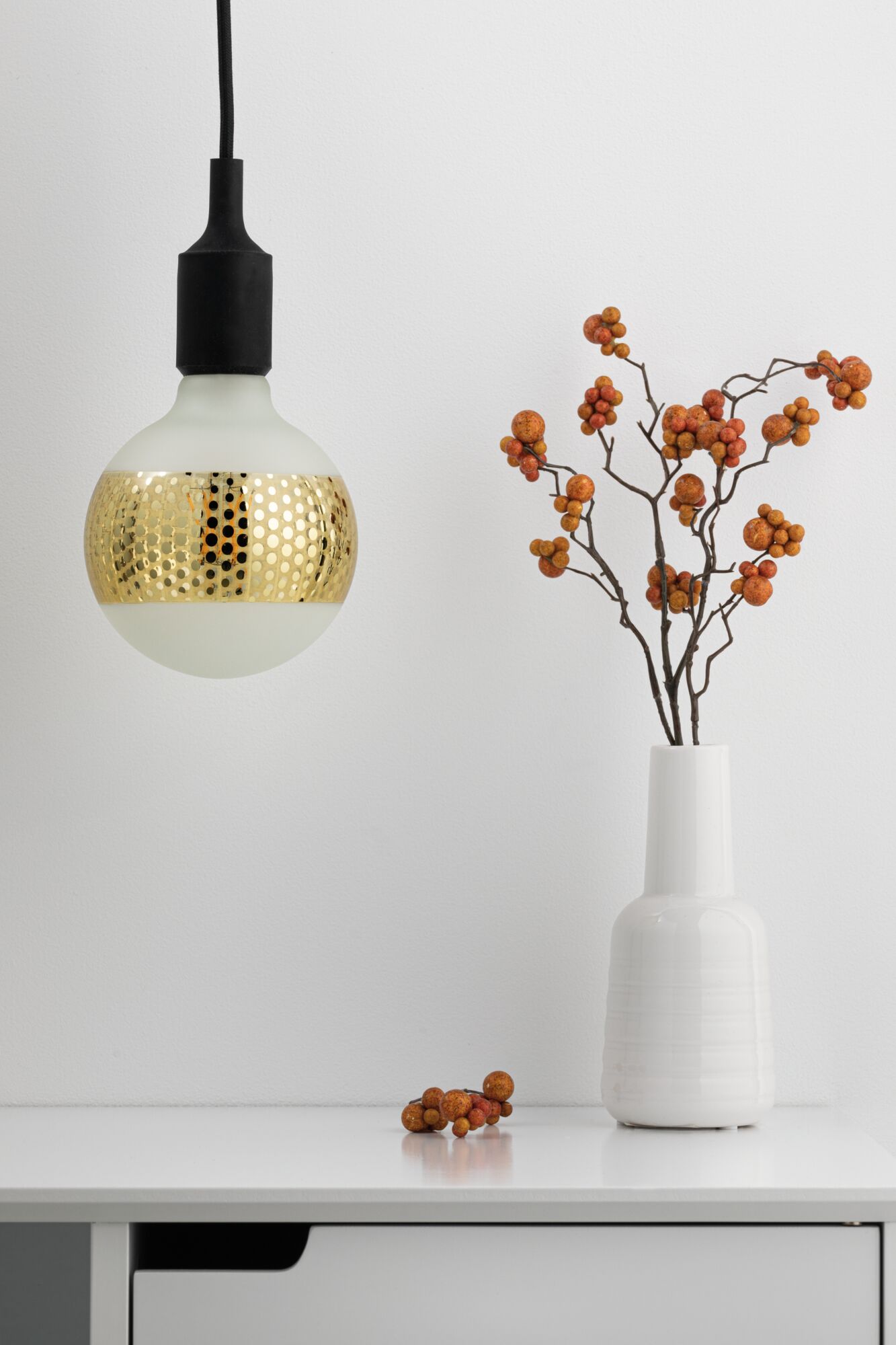 Modern pendant light with matte white glass bulb and gold perforated band, minimalist interior lighting.
