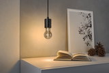 Schwarze Pendelleuchte mit klarer Glühbirne über weißem Tisch mit Buch und Deko im Wohnzimmer