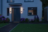 Moderne husindgang med mørk dør og to slanke væglamper med varmt hvidt LED-lys udenfor.