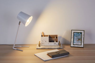 Witte metalen bureaulamp met warm licht op houten bureau naast marmeren organizer en fotolijst