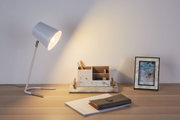 Hvid metal skrivebordslampe med varmt lys på træbord ved siden af marmor organizer og billedramme