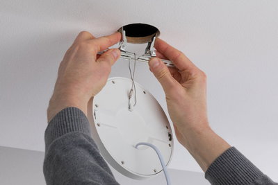 Hände montieren weißen LED-Einbaustrahler mit Metallfedern in Deckenöffnung für moderne Beleuchtung