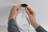 Hände montieren weißen LED-Einbaustrahler mit Metallfedern in Deckenöffnung für moderne Beleuchtung