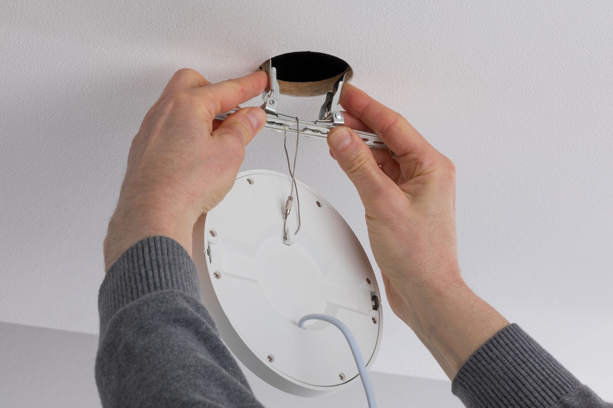 Hands installing white LED recessed spotlight with metal springs into ceiling hole for modern lighting