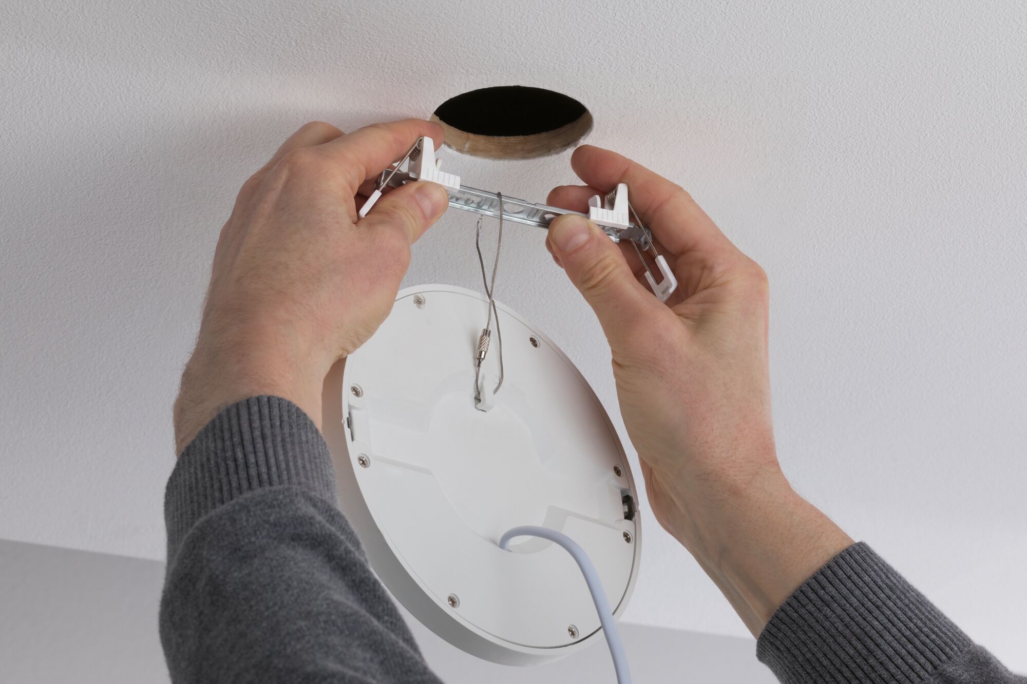 Mains installant un spot LED encastré blanc avec ressorts métalliques dans un trou de plafond moderne