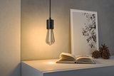 Zwarte hanglamp met warmwit LED-filament boven wit dressoir met boek en decoratie.