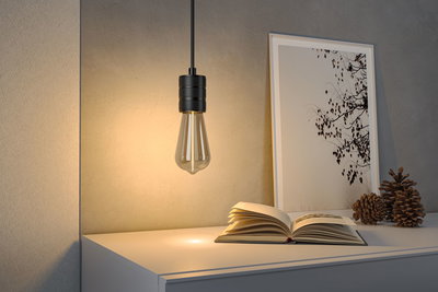Suspension noire avec filament LED blanc chaud au-dessus d'un buffet blanc avec livre et déco.