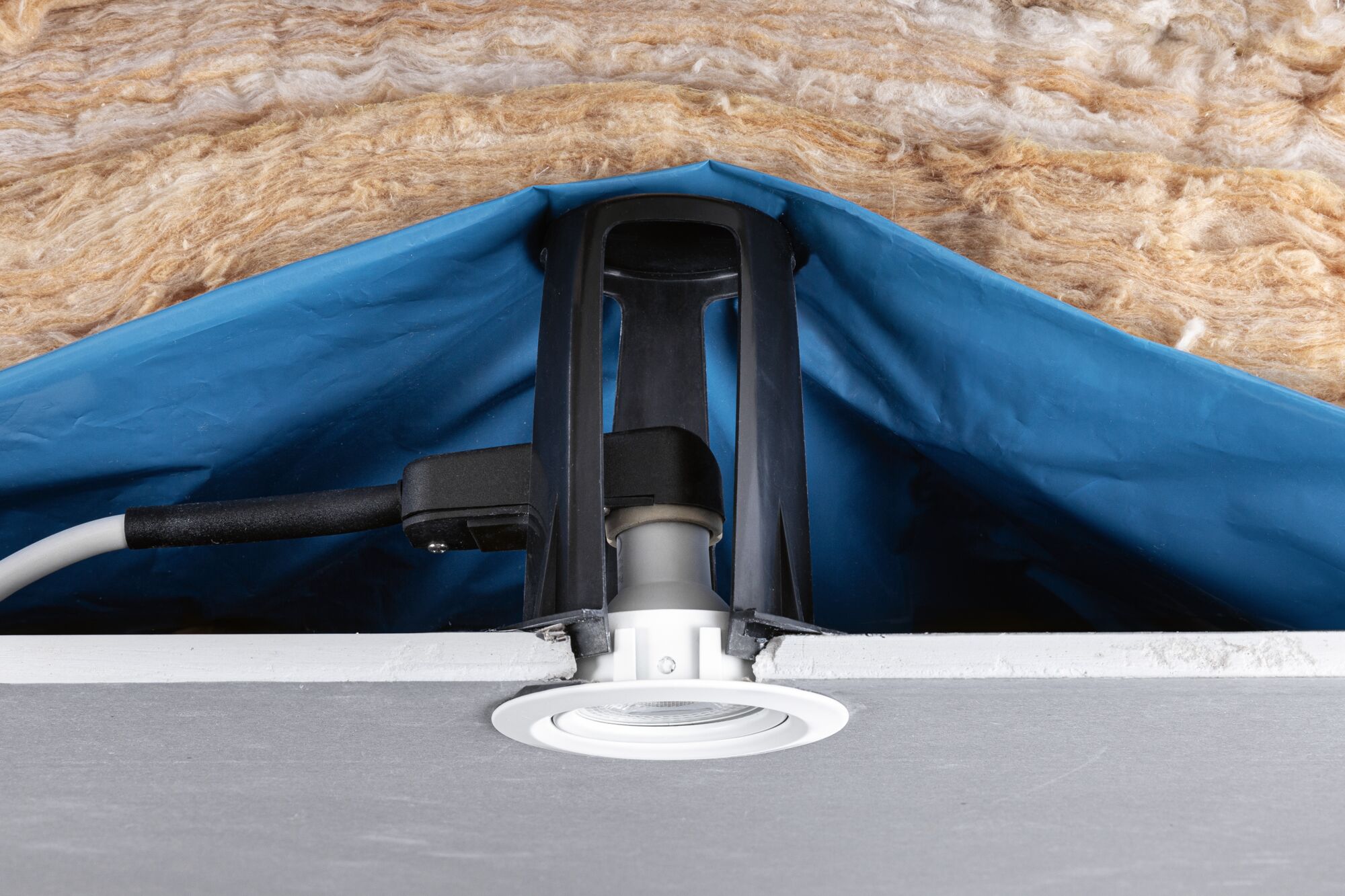 White plastic recessed spotlight with black bracket in suspended ceiling with insulation material