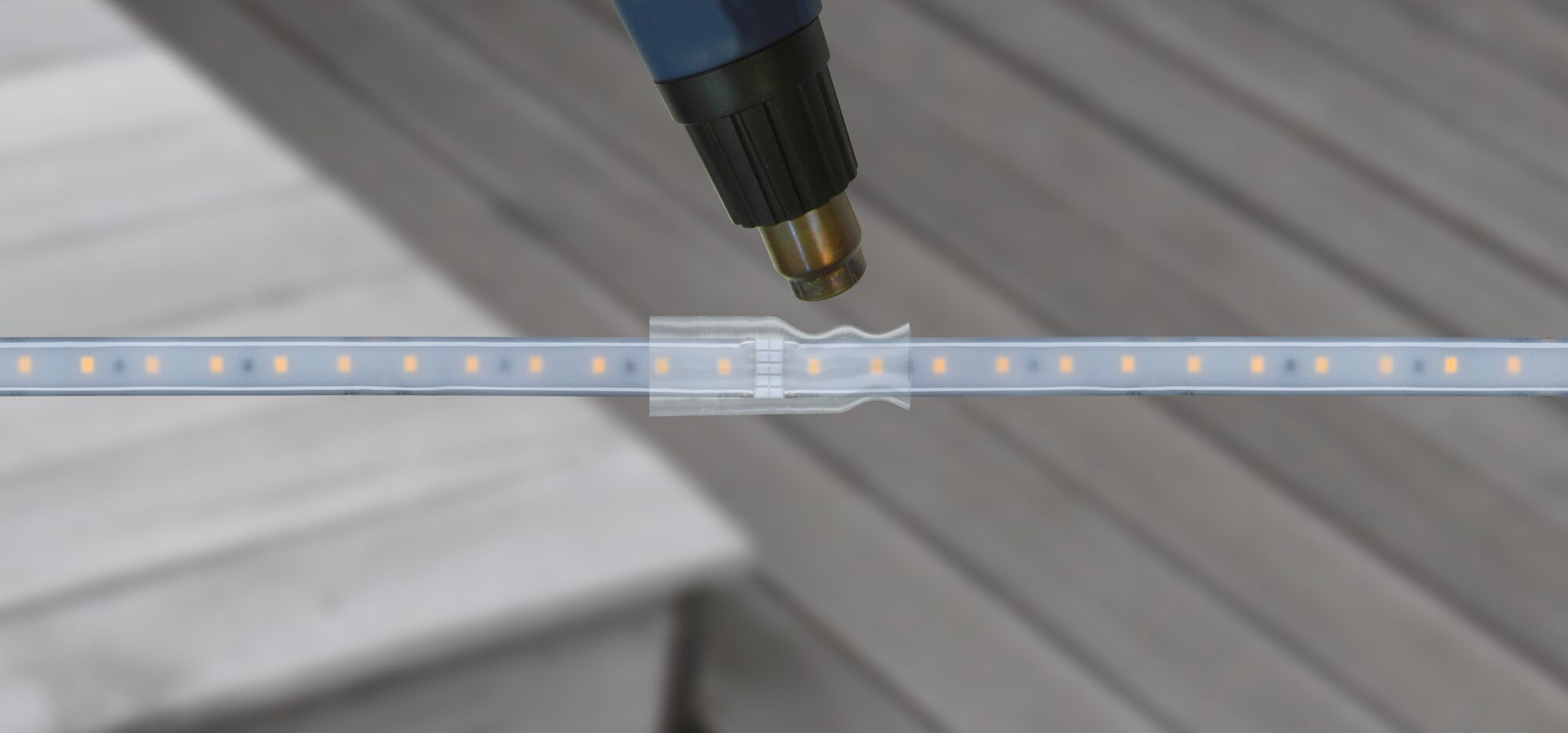 Nahaufnahme eines LED-Streifen mit transparentem Verbinder und Heißluftfön zum Schrumpfen der Isolierung